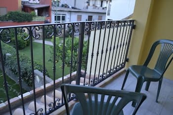 A serene balcony with ornate metal railings overlooks a lush green garden, featuring green plastic chairs perfect for relaxing, ideal for travelers seeking a peaceful urban retreat.