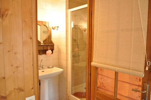 A cozy cabin-style bathroom with wooden walls, a pedestal sink, a glass-enclosed shower, and floral-patterned blinds creates a warm and inviting atmosphere, perfect for travelers seeking rustic charm in their accommodations.