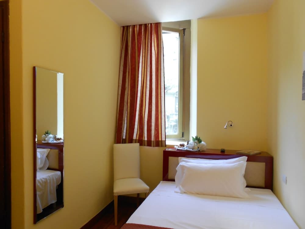 A cozy hotel room with yellow walls, a neatly made bed, striped curtains, and a small desk adorned with flowers, ideal for travelers seeking comfort and simplicity.