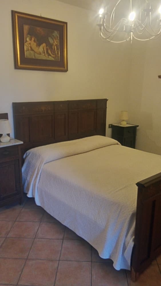 A cozy bedroom with tiled floors, wooden furniture, and a chandelier exudes warmth and charm, ideal for travelers seeking a serene and elegant accommodation experience.