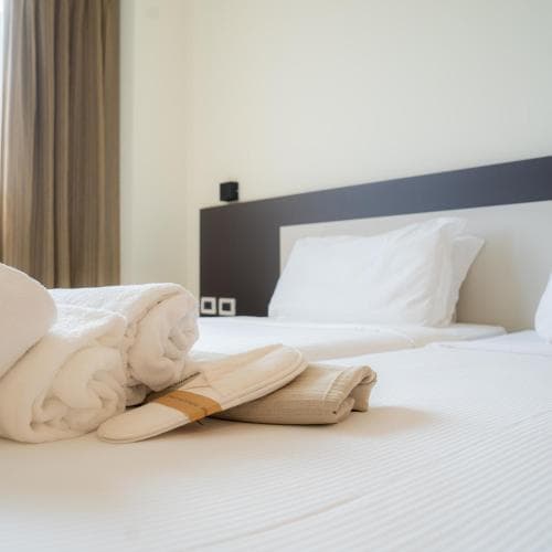 A cozy hotel room features a neatly made bed with white linens, rolled towels, and slippers, creating a welcoming atmosphere ideal for travelers seeking comfort and relaxation.