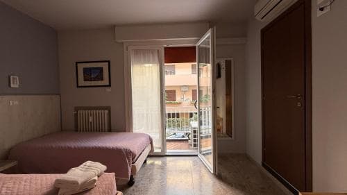 A cozy hotel room with a neatly made bed, soft lighting, and an open door leading to a balcony with outdoor seating, perfect for travelers seeking relaxation and comfort.