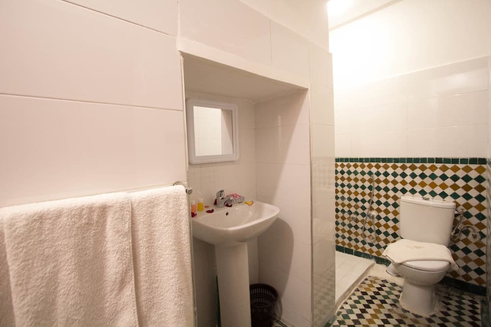 A cozy bathroom with white tiled walls, a colorful mosaic-tiled shower area, and neatly hung towels offers a clean and inviting space for travelers seeking comfort during their stay.