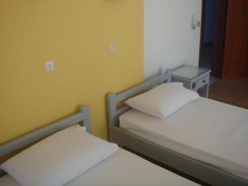 A cozy guesthouse room features two single beds with white linens against a vibrant yellow wall, creating a warm and inviting atmosphere ideal for budget travelers seeking simple accommodations.