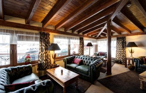 A cozy lounge with plush leather sofas, wooden beams, and patterned curtains offers a warm and inviting atmosphere ideal for relaxation in a boutique hotel setting.
