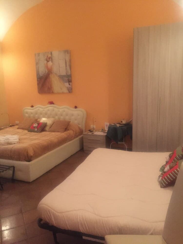 A cozy bedroom with warm orange walls, a tufted bed adorned with pillows, a futon mattress, and a painting of a woman in a dress creates an inviting atmosphere ideal for travelers seeking comfortable accommodation.