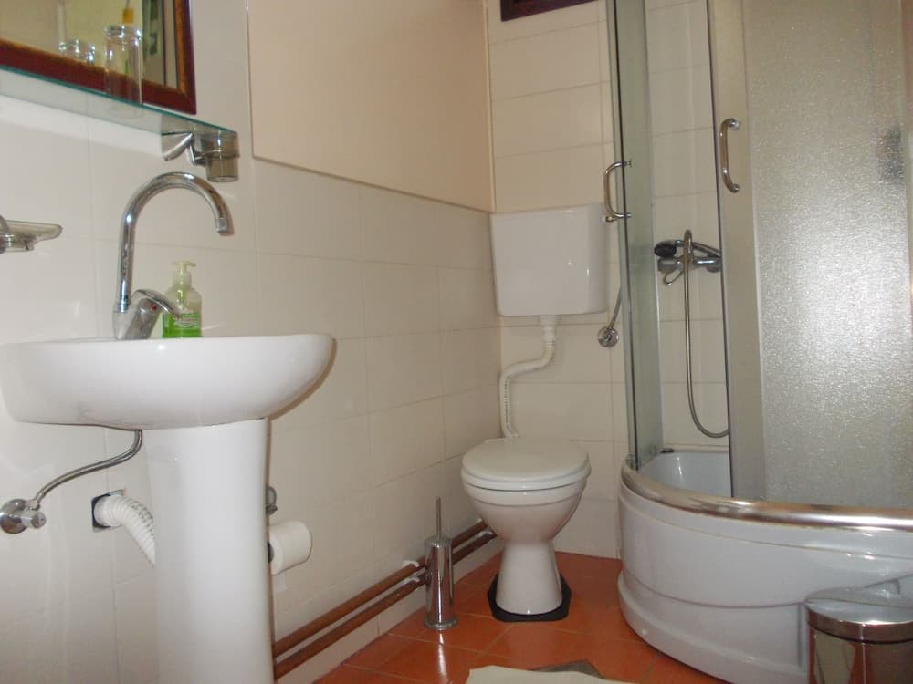 A cozy bathroom with white tiled walls, a pedestal sink, a toilet, and a shower enclosure, featuring warm terracotta flooring and a modern aesthetic, ideal for travelers seeking comfort in compact spaces.
