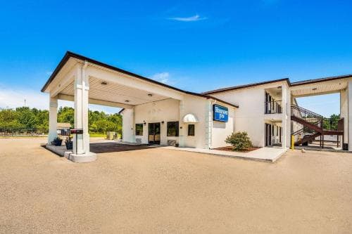 A sunny day highlights the welcoming entrance of a roadside motel with a covered driveway, white pillars, and a staircase leading to an upper level, ideal for travelers seeking convenient lodging.
