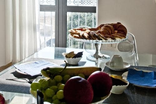 A cozy breakfast setup with fresh fruits and pastries on a glass table by a window with a balcony view, ideal for a relaxing morning in a charming hotel room.