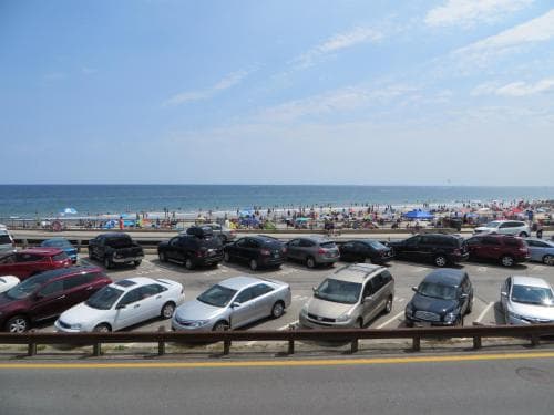 A bustling beach scene with parked cars along the roadside under a clear blue sky, ideal for travelers seeking coastal relaxation and vibrant seaside activities.