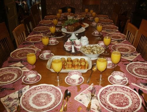 A cozy dining room set for a festive meal features a long table adorned with patterned plates, glasses of orange juice, and an array of appetizers, perfect for capturing the warmth and charm of a family gathering or holiday celebration.