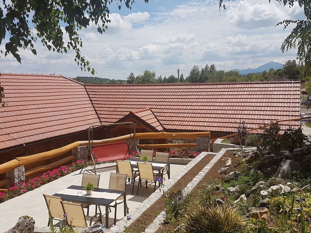 A serene outdoor patio with wooden railings, tiled roofs, and vibrant flower beds offers a tranquil retreat under a partly cloudy sky, ideal for travelers seeking relaxation in a picturesque countryside setting.