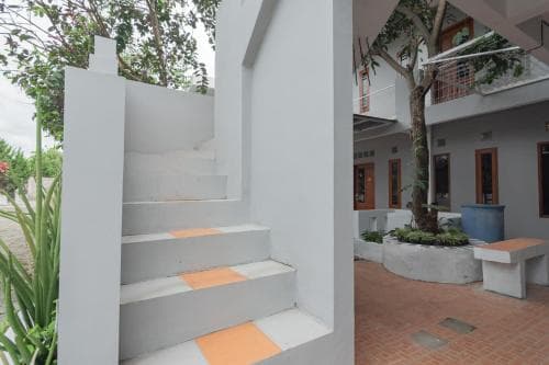 A serene courtyard with white walls, orange-accented steps, and lush greenery creates an inviting atmosphere ideal for a tranquil getaway at a boutique hotel.
