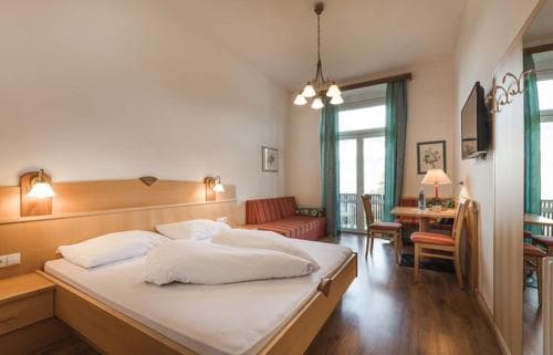 A cozy hotel room with warm lighting, wooden floors, a neatly made bed, and a balcony view offers a comfortable retreat for travelers seeking relaxation.