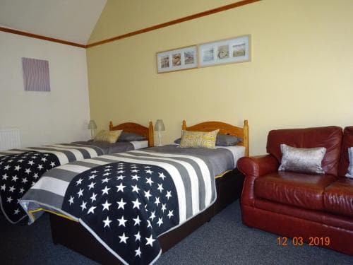 A cozy guesthouse room features two single beds adorned with star-patterned blankets, a red leather sofa, and framed artwork on the walls, ideal for travelers seeking a comfortable and inviting stay.