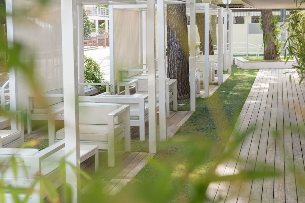 A serene outdoor seating area features white lounge chairs under sheer canopies, surrounded by lush greenery and wooden pathways, ideal for relaxing retreats or upscale resort stays.