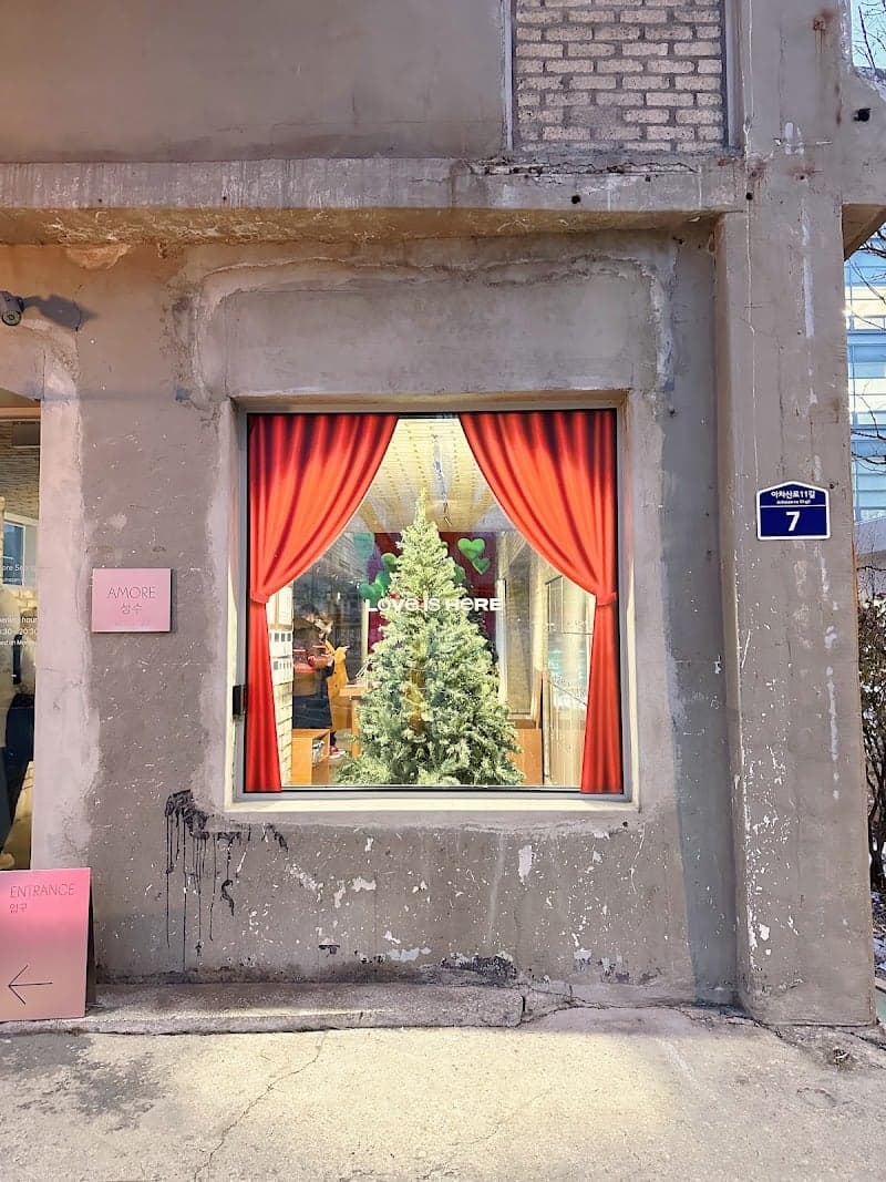 A charming urban storefront in Seoul, South Korea, features a festive window display with red curtains framing a Christmas tree, evoking a cozy holiday atmosphere ideal for seasonal shopping and photography.