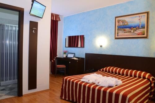 A cozy hotel room with a neatly made striped bed, blue walls adorned with a seaside painting, and warm lighting creates an inviting atmosphere ideal for travelers seeking comfort and relaxation.