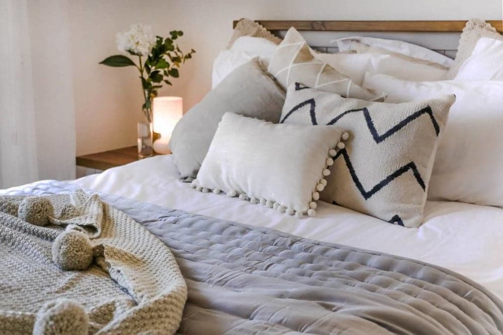 A cozy bedroom scene featuring a neatly arranged bed with soft textiles, decorative pillows, and a warm ambiance from a glowing bedside lamp, ideal for travelers seeking comfort and relaxation.