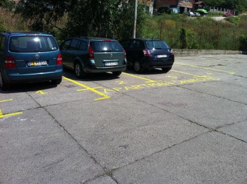A quiet parking lot with three cars parked in designated spots under the shade of trees, ideal for travelers seeking a peaceful layover spot near residential areas.