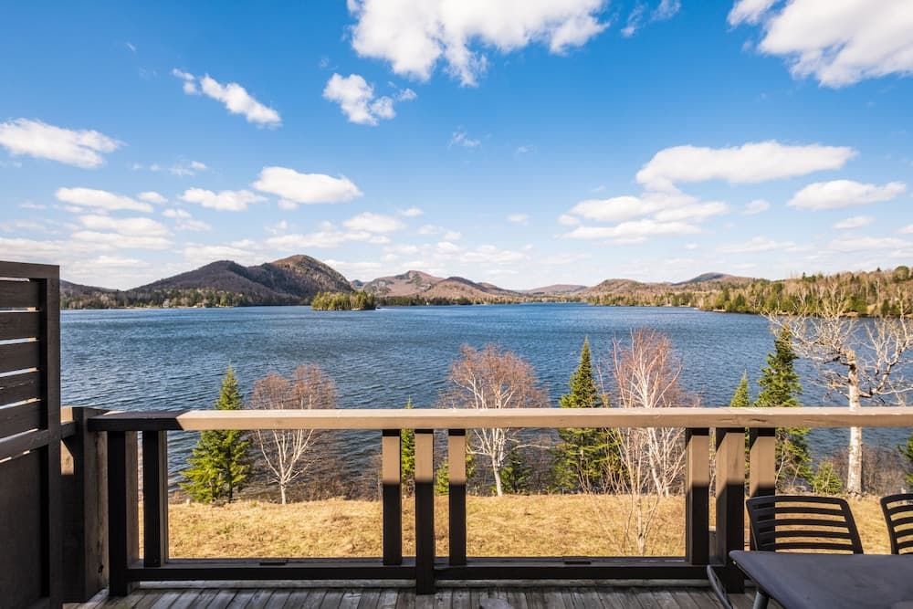 A serene lakeside deck offers breathtaking views of calm waters, distant hills, and scattered trees under a partly cloudy sky, ideal for tranquil retreats and nature photography.