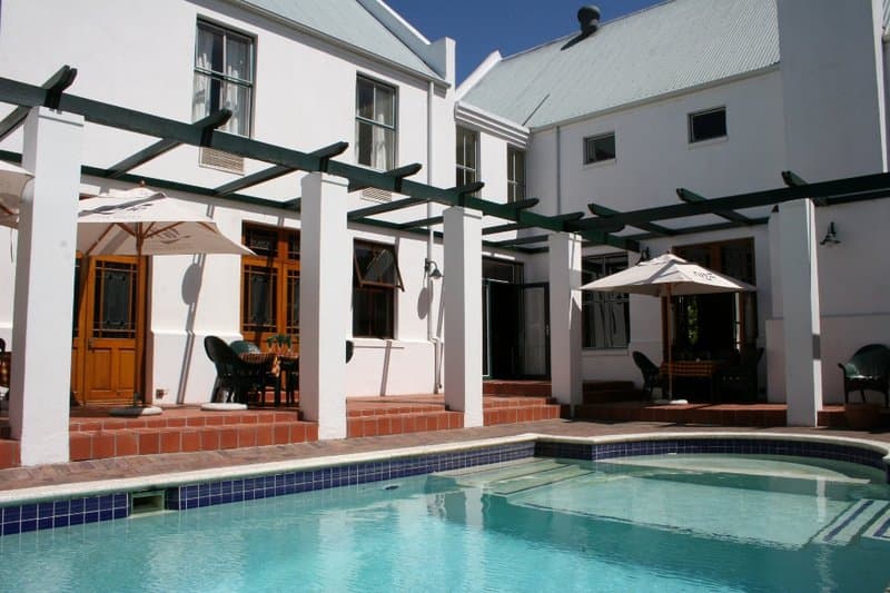 A serene courtyard with a sparkling pool, white pergola, and cozy seating areas invites travelers to relax in a charming villa setting.