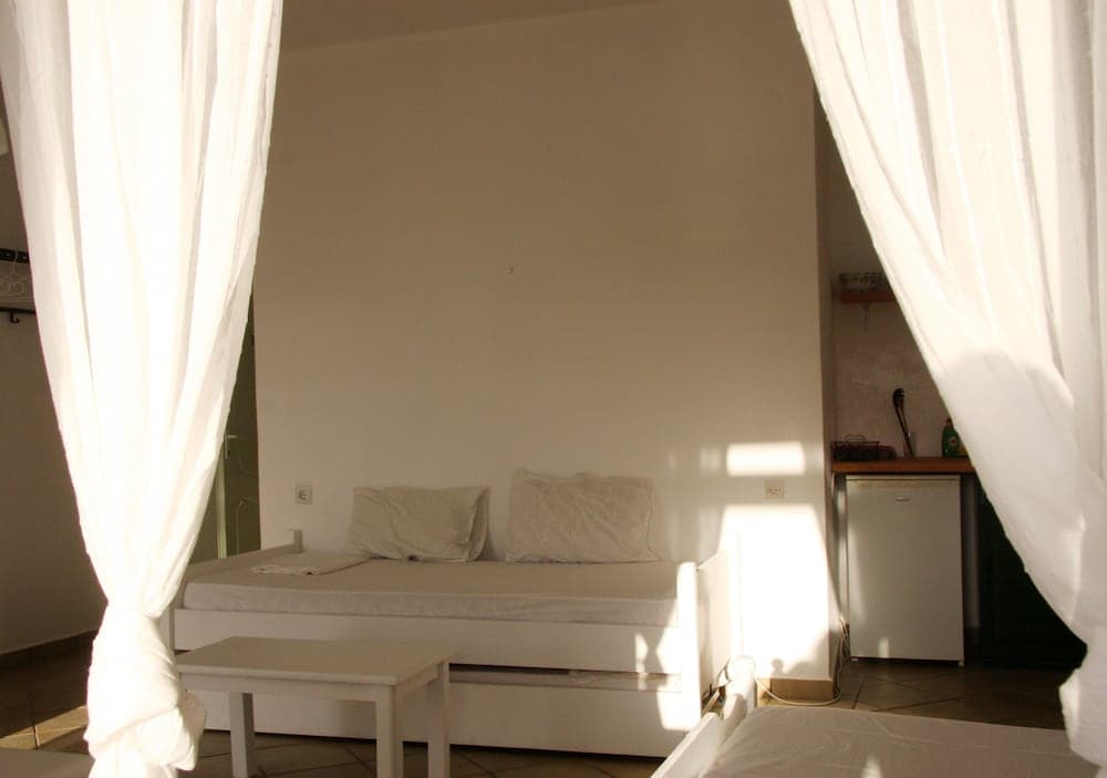 A cozy, minimalist bedroom with white curtains framing the space, featuring a simple bed setup, a small table, and soft natural light, ideal for travelers seeking a serene and budget-friendly accommodation.
