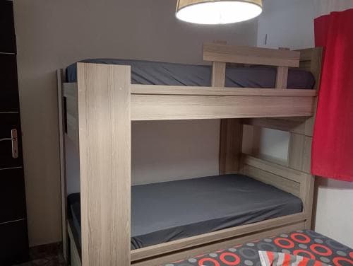 A cozy hostel room features a wooden bunk bed with gray mattresses under warm lighting, ideal for budget travelers seeking comfortable accommodations.