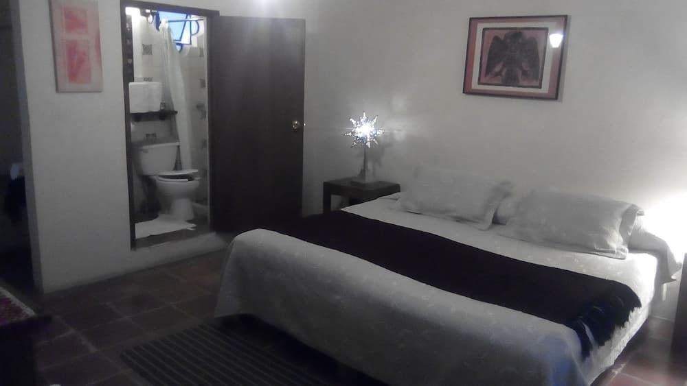 A cozy hotel room with a neatly made bed adorned with a black throw blanket, a sparkling star decoration on the nightstand, and an open bathroom door revealing a toilet, ideal for travelers seeking comfort and convenience.