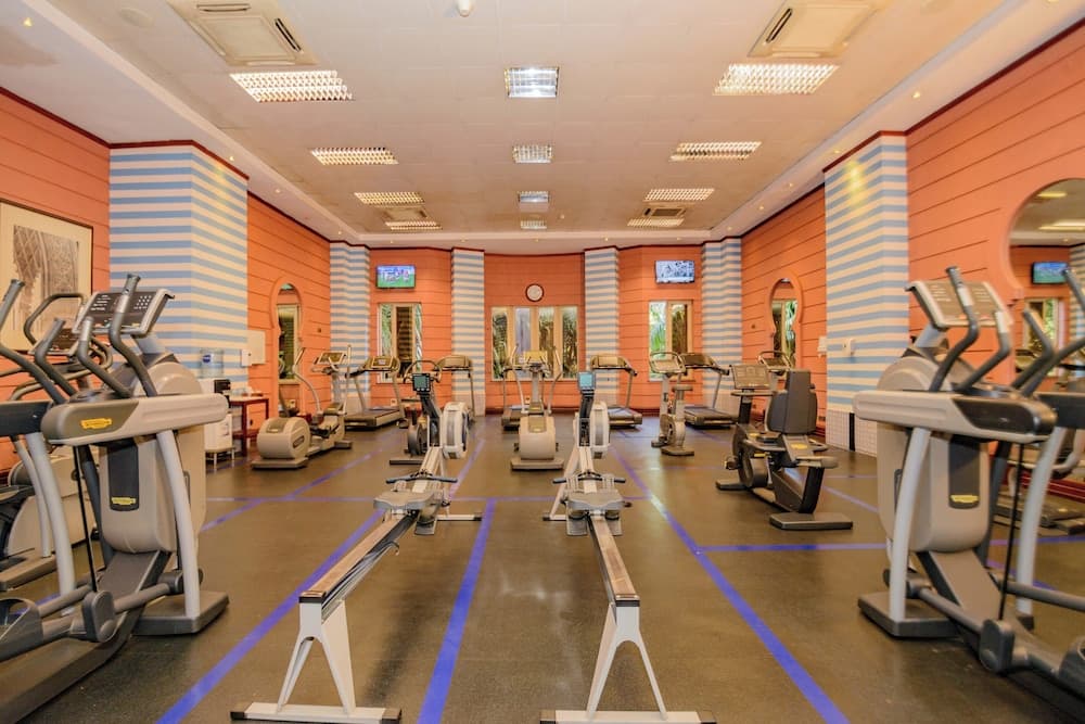 A brightly lit indoor gym with orange and blue striped walls, featuring treadmills, ellipticals, and rowing machines, offers a vibrant and modern fitness environment ideal for travelers seeking a workout during their stay.