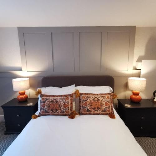 A cozy hotel room features a neatly made bed adorned with patterned cushions, flanked by matching bedside tables with orange lamps, creating a warm and inviting atmosphere ideal for travelers seeking comfort.