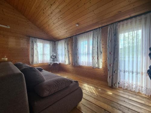 A cozy wooden cabin interior with a plush sofa, lace curtains, and natural light streaming through large windows, ideal for a serene getaway retreat.
