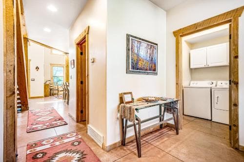 A cozy interior hallway with rustic wooden accents, vibrant rugs, and a laundry area leads to a warmly lit dining space, ideal for travelers seeking a comfortable and inviting vacation rental.