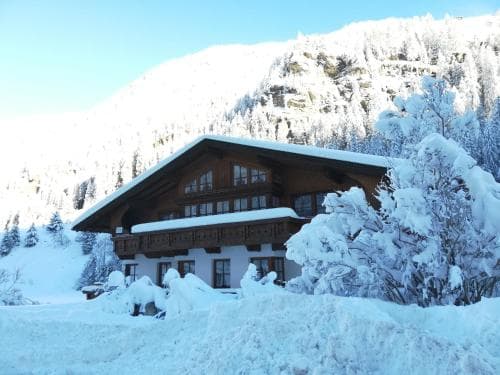 A serene winter scene showcases a cozy chalet nestled among snow-covered trees and mountains, ideal for a peaceful ski retreat.