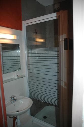 A modern bathroom with a sleek glass shower enclosure and a white sink set against orange and gray walls, ideal for travelers seeking a clean and stylish accommodation space.