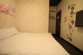 A cozy hotel room features a neatly made bed against floral wallpaper, adorned with wall art and a flat-screen TV, ideal for travelers seeking comfort in a compact space.
