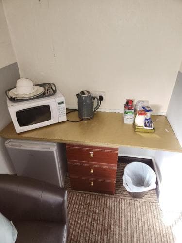 A cozy hotel room corner features a microwave, mini fridge, and small desk with essentials like coffee supplies, evoking a practical and comfortable stay for travelers seeking convenience.