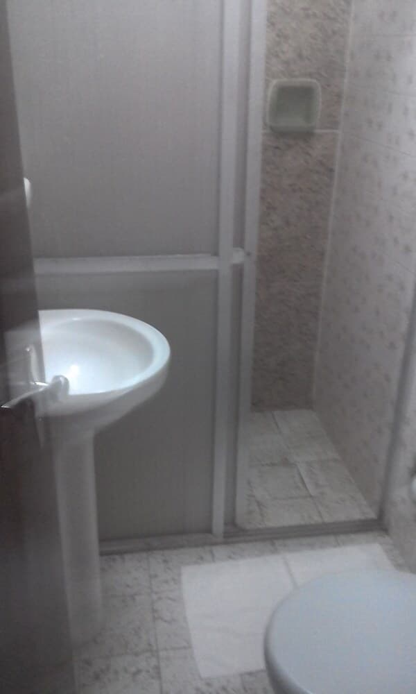 A compact bathroom with a pedestal sink, glass-enclosed shower, tiled walls, and a toilet creates a functional space ideal for travelers seeking efficient accommodations.