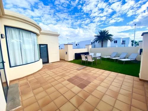 A sunny rooftop terrace with tiled flooring, lounge chairs, artificial grass, and a palm tree offers a relaxing retreat for travelers seeking a cozy vacation spot.
