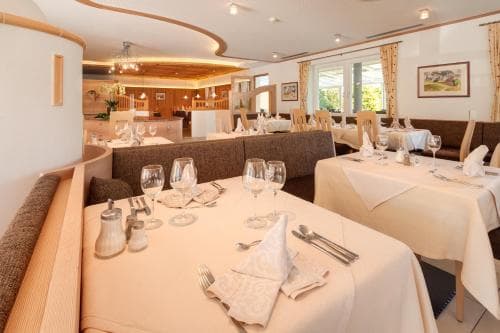 A cozy restaurant with warmly lit tables set for dining, featuring elegant glassware and neatly folded napkins, creates an inviting atmosphere perfect for travelers seeking a comfortable dining experience.