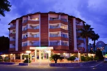 A vibrant evening view of a modern hotel with illuminated balconies and palm trees, creating a welcoming atmosphere ideal for travelers seeking a cozy stay in a tropical destination.