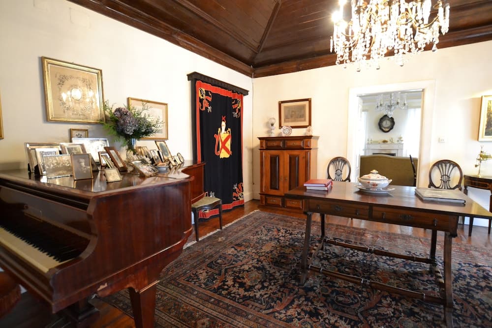 An elegantly furnished historic room features a grand piano, ornate chandelier, antique furniture, and a vibrant tapestry, creating a sophisticated atmosphere ideal for cultural heritage tourism.