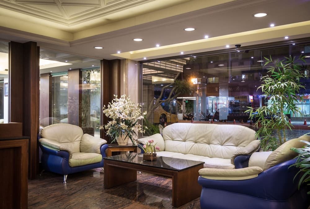 A cozy hotel lobby features plush blue and cream leather seating around a glass-topped coffee table, adorned with fresh flowers and greenery, creating a welcoming atmosphere ideal for travelers seeking relaxation.