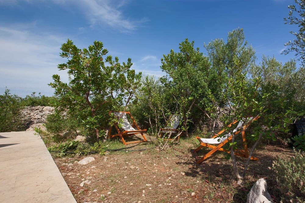 A serene outdoor retreat features orange lounge chairs nestled among lush greenery under a clear blue sky, ideal for relaxing vacations in a tranquil garden setting.