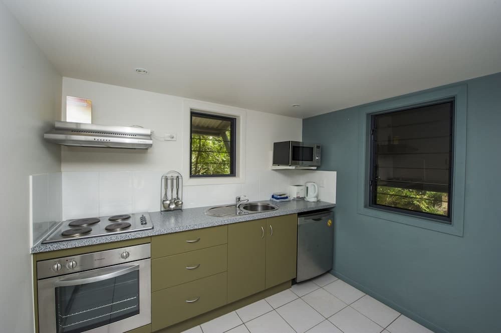 A cozy, modern kitchen with stainless steel appliances, green cabinetry, and windows offering a serene view of greenery, ideal for travelers seeking self-catering accommodations.