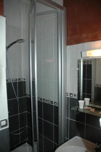 A modern bathroom with black tiled walls, a glass-enclosed shower, and a sleek sink under a mirror creates a clean and functional space ideal for travelers seeking comfort in accommodations.