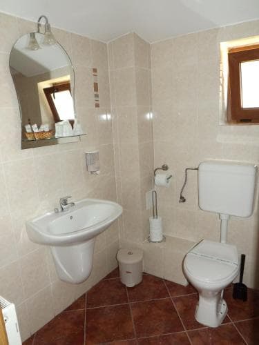 A cozy bathroom with beige tiled walls, a sink, toilet, bidet, and a small window, exudes a warm and inviting atmosphere ideal for travelers seeking comfort in their accommodations.