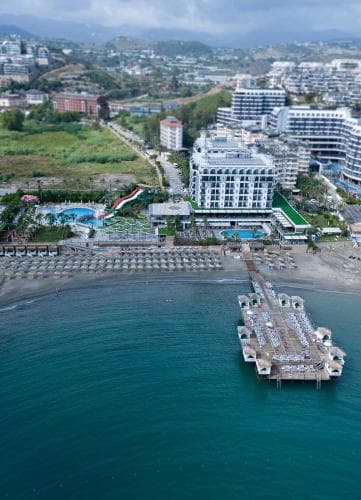 An aerial view captures a vibrant coastal resort with lush greenery, modern buildings, and a serene beachfront, ideal for travelers seeking luxury and relaxation by the sea.