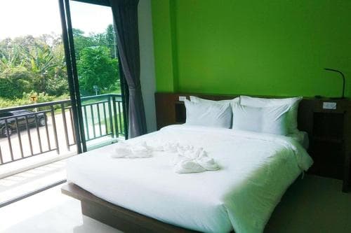 A cozy bedroom with a vibrant green wall and a neatly made bed overlooks lush greenery through a sliding glass door, ideal for travelers seeking relaxation in a serene, tropical setting.