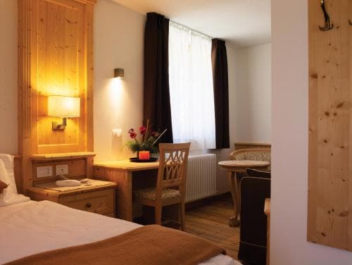 A cozy hotel room with wooden accents, warm lighting, and a neatly arranged desk featuring flowers creates an inviting atmosphere ideal for travelers seeking comfort and relaxation.